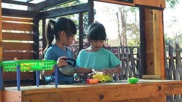 Happy sisters play with food and wooden grocery toys at the outdoor playground with her mother. Cute Asian girl roleplaying selling fruit juice at the park. Family spending time together on vacation.