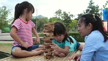 niños emocionados y mamá jugando al juego de bloques de madera de la torre jenga juntos en el parque. familia feliz con niños disfrutando juntos de las actividades de fin de semana. video