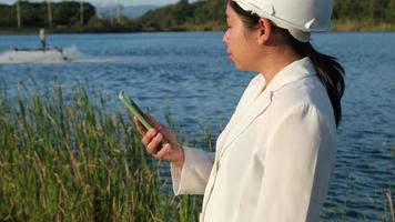 Environmental engineer wearing a white helmet uses a mobile phone to record data analyzing oxygen levels in a reservoir. Water and ecology concept. video