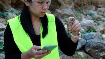 femmina geologo utilizzando mobile Telefono per disco dati analizzando rocce o ghiaia. ricercatori raccogliere campioni di biologico materiali. ambientale e ecologia ricerca. video