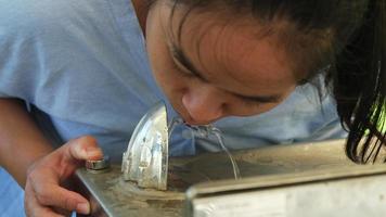 Young Asian woman drinking water from a drinking fountain in the park. video