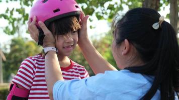 Young mother helps her daughter put on her protection pads and helmet before roller skating in the park. Active leisure and outdoor sport for child. video