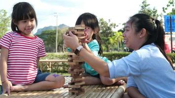 Aufgeregte Kinder und Mutter spielen gemeinsam Jenga-Tower-Holzblockspiel im Park. glückliche familie mit kindern, die gemeinsam wochenendaktivitäten genießen. video