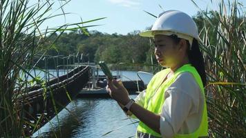 milieu ingenieur vervelend een wit helm toepassingen een mobiel telefoon naar Vermelding gegevens analyseren zuurstof niveaus in een reservoir. water en ecologie concept. video