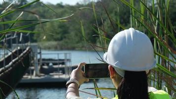 engenheiro ambiental usando um capacete branco usa um telefone celular para gravar dados analisando os níveis de oxigênio em um reservatório. conceito de água e ecologia. video