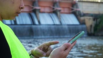 Female environmentalist uses a mobile phone to take pictures and record data analyzing the dam's water for contaminants. Water and ecology concept. video