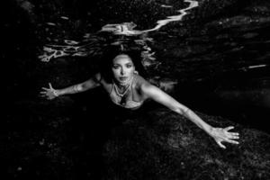 Mermaid swimming underwater in the deep blue sea in black and white photo
