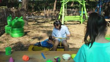 irmãs felizes brincam com comida e brinquedos de mercearia de madeira no playground ao ar livre com a mãe. linda garota asiática interpretando vendendo suco de frutas no parque. família passando tempo juntos nas férias. video