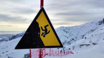signo símbolo del peligro de caer del acantilado de las montañas con nieve durante el invierno en la estación de esquí. tenga cuidado al esquiar, manténgase en las pistas marcadas. actividades y deportes de invierno.