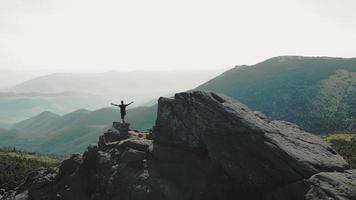 A man standing on top of a mountain with and raising his hands up the mountain. Victory and overcoming the top. A tourist looking at the sunrise on top of a rock. video