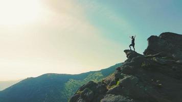 um homem de pé no topo de uma montanha e levantando as mãos para cima da montanha. vitória e superação do topo. um turista olhando o nascer do sol em cima de uma rocha. video