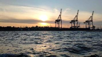 tramonto Visualizza di il mare carico porta e contenitore terminale di Odessa. navi Caricamento in corso di gru nel il sera contro il fondale di il ambientazione sole. Visualizza a partire dal mare su barca. video
