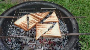 rostat bröd bröd för smörgåsar varelse tillverkad på en lägereld i trädgård. hemlagad rostat fullkorn bröd på de grill galler. små gyllene rostat bröd. video