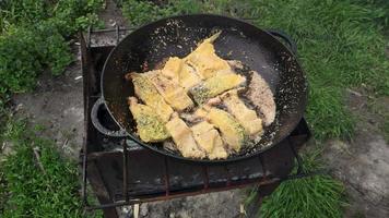 Roasting juicy salmon with spices and herbs in burning charcoals fire on BBQ pan. Breaded smoked fish on fire. Man hand put a piece of fish in a frying pan. Grilled food in camping on picnic in summer video