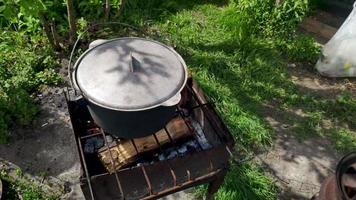 Large cauldron with a lid on a fire. Big vat with food cooking on a campfire. The cast iron pot stands on the grill brazier in windy weather. Outdoor cooking.