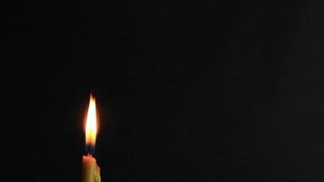 un primer plano de una vela encendida con llama amarilla, una luz de vela en la oscuridad, se quema y después de un rato una ráfaga de viento la apaga. video