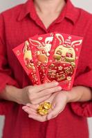 mujer sosteniendo un sobre rojo chino con lingotes de oro, regalo de dinero para felices vacaciones de año nuevo lunar. frase china significa felicidad, salud, suerte y riqueza foto