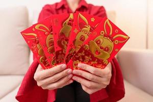 woman holding Chinese red envelope with golden rabbit and blessing word, money gift for happy Lunar New Year holiday. Chinese sentence means happiness, healthy, Lucky and Wealthy photo