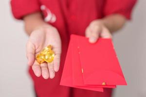 Woman holding Chinese red envelope with gold bullion, money gift for happy Lunar New Year holiday. Chinese sentence means happiness, healthy, Lucky and Wealthy photo