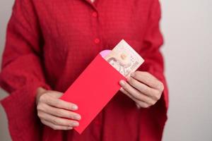 mujer sosteniendo un sobre rojo chino con regalo de dinero en baht tailandés para felices vacaciones de año nuevo lunar foto