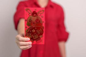 woman holding Chinese red envelope with golden rabbit and blessing word, money gift for happy Lunar New Year holiday. Chinese sentence means happiness, healthy, Lucky and Wealthy photo