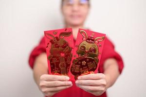 mujer sosteniendo un sobre rojo chino con conejo dorado y palabra de bendición, regalo de dinero para felices vacaciones de año nuevo lunar. frase china significa felicidad, salud, suerte y riqueza foto