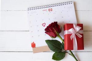 Red rose and red gift box on calendar isolated on white wooden background with. Valentine's day concept. Planning scheduling agenda, Event, organiser valentines day. Flat lay, top view. photo