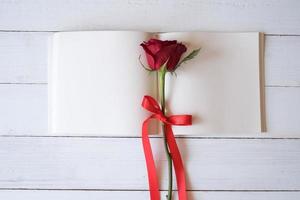 Blank notebook with red roses on wooden table. Copy space for your text. Valentine's day, wedding, birthday and special occasion concept. Copy space for text. Top view, Flat lay. photo