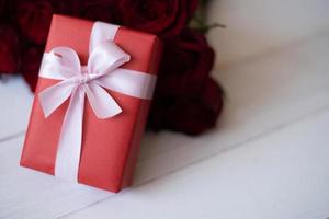 Close up red gift box with bunch of rosy roses blurred background. Valentine's day, wedding, birthday and special occasion concept. Copy space for text. photo