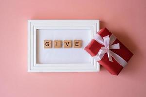 Red gift box and photo frame with letter words of give on pink background for giving in holidays with copy space for text. Holidays, present, giving. New year day, Christmas day, Chinese New Year.