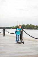 A boy on a scooter along the embankment of the city. Journey. Backpack on the back. The face expresses natural joyful emotions. Not staged photos from life