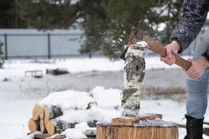 A man is chopping firewood with an axe in winter outdoor in the snow. Alternative heating, wood harvesting, energy crisis photo