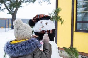 un niño pinta la cara de un muñeco de nieve con pinturas: entretenimiento y creatividad invernales, esculpiendo un muñeco de nieve en invierno al aire libre. foto