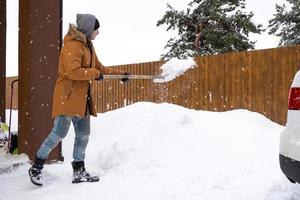 A man in winter cleans snow with a shovel in the yard of a house in the parking lot. Snowfall, difficult weather conditions, the car is stalling, digging up the passage photo