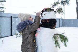 A child paints a snowman's face with paints - winter entertainment and creativity, sculpting a snowman in winter outdoor. photo