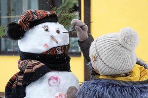 A child paints a snowman's face with paints - winter entertainment and creativity, sculpting a snowman in winter outdoor. photo