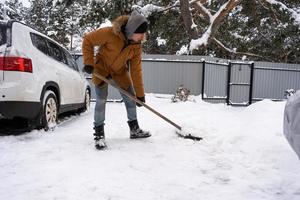 un hombre en invierno limpia la nieve con una pala en el patio de una casa en el estacionamiento. nevadas, condiciones climáticas difíciles, el automóvil se está estancando, excavando el pasaje foto