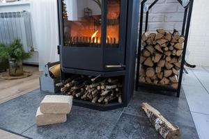 Fuel briquettes made of pressed sawdust for kindling the furnace - economical alternative eco-friendly fuel for the fireplace in the house. Firewood is burning in the oven in the interior photo
