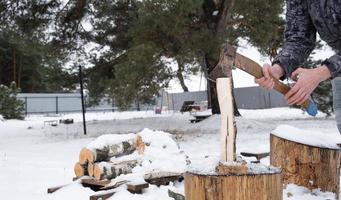 A man is chopping firewood with an axe in winter outdoor in the snow. Alternative heating, wood harvesting, energy crisis photo