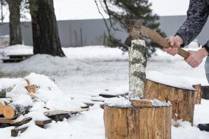 A man is chopping firewood with an axe in winter outdoor in the snow. Alternative heating, wood harvesting, energy crisis photo