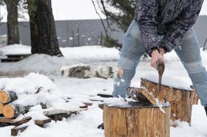 A man is chopping firewood with an axe in winter outdoor in the snow. Alternative heating, wood harvesting, energy crisis photo