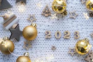 Happy New Year-wooden letters and the numbers 2023 on festive white knitted background with sequins, stars, lights of garlands. Greetings, postcard. Calendar, cover photo