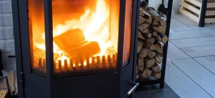 Fuel briquettes made of pressed sawdust for kindling the furnace - economical alternative eco-friendly fuel for the fireplace in the house. Firewood is burning in the oven in the interior photo