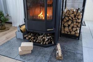 Fuel briquettes made of pressed sawdust for kindling the furnace - economical alternative eco-friendly fuel for the fireplace in the house. Firewood is burning in the oven in the interior photo