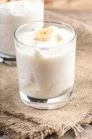 Traditional homemade yogurt with banana slices in transparent glasses on burlap napkin. photo