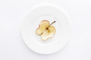 One thin slice of dried apple on round white plate on white background. photo