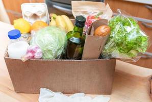 Close-up cardboard box with fresh packed food products on wooden kitchen table. Safe delivery concept. Selective focus. photo