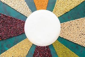 Legumes and cereals is laid out like sun rays on emerald background with round plate in center. photo