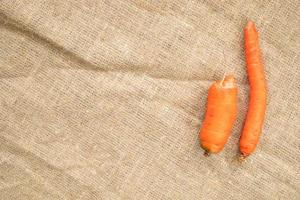 Two non-standard ugly carrots thin crooked and small on burlap . photo