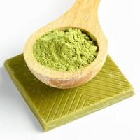 Close-up wooden spoon of japanese matcha tea powder and one slice of unusual green chocolate with matcha on white. photo
